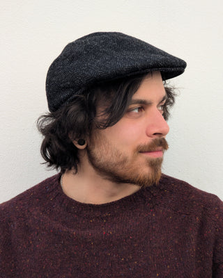 Zu sehen ist eine Schiebemütze aus Harris Tweed in Schwarzgrau von der Seite aus betrachtet.