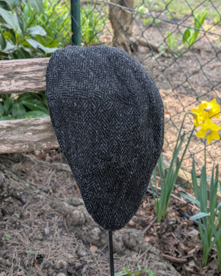 Zu sehen ist eine Schiebemütze aus Harris Tweed in Schwarzgrau bei Tageslicht.