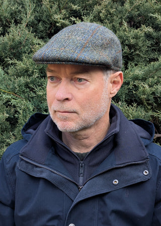 Die Schiebermütze aus original Harris Tweed in oliv blau Tönen basiert auf einem Fischgrätmuster mit zusätzlichen Einträgen in Kette und Schuss.