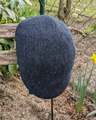 Zu sehen ist eine Schiebermütze aus original Harris Tweed in klassisch dunklem blauen Fischgrätmuster. Die Passform ist gut geschnitten über die Kalotte.