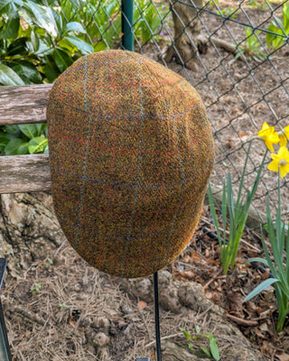 Zu sehen ist eine Schiebermütze aus Harris Tweed in rostbraunem Gewebe mit zusätzlichen Einträgen in Rot, Orange, Blau und Petrol. 