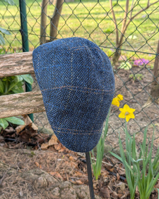 Klassische Schiebermütze mit original Harris Tweed. Der Oberstoff ist in Fischgrätmuster gewebt. Zusätzliche Einträge in orange, hellgrau und mittelblau ergeben einen erfrischenden Struktureffekt.