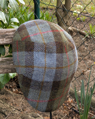 Von oben betrachtet die Schiebermütze aus Harris Tweed in den Farben hellblau, hellgrün, braun mit roten und curry farbenen Streifen.