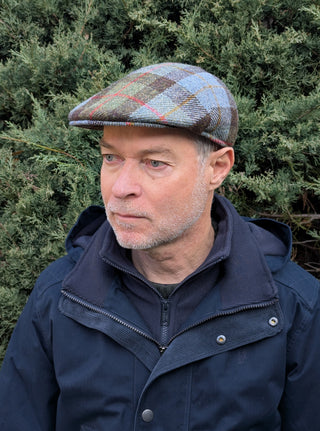 Zu sehen ist eine Schiebermütze aus Harris Tweed in den Farben hellblau, hellgrün, braun mit roten und curryfarbenen Streifen. Das Highland Check Muster ist besonders anspruchsvoll zu weben und lässt sich vielseitig kombinieren. Karos sind typisch für schottisches Design.