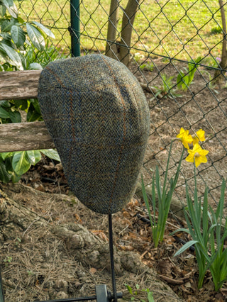 Zu sehen ist eine Schiebermütze aus Harris Tweed in den Farben oliv mit blau