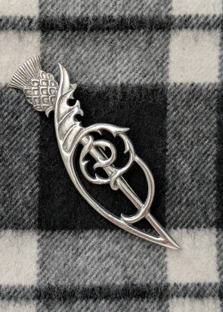 Zu sehen ist eine traditionelle schottische Kiltnadel (kilt pin) mit Distel und keltischem Flechtmotiv